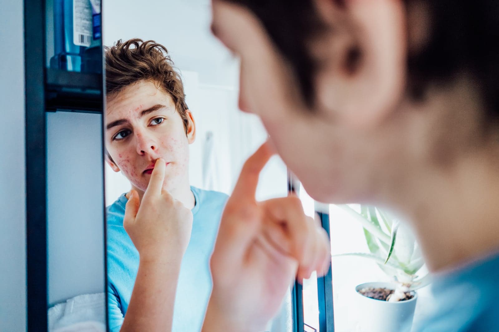 Teen examining acne in a bathroom mirror before school